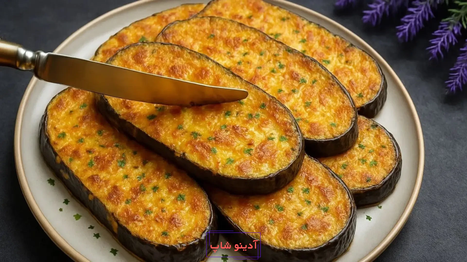 برش‌های بادمجان تنوری با روکش پنیر برشته و جعفری خرد شده در بشقاب سفید