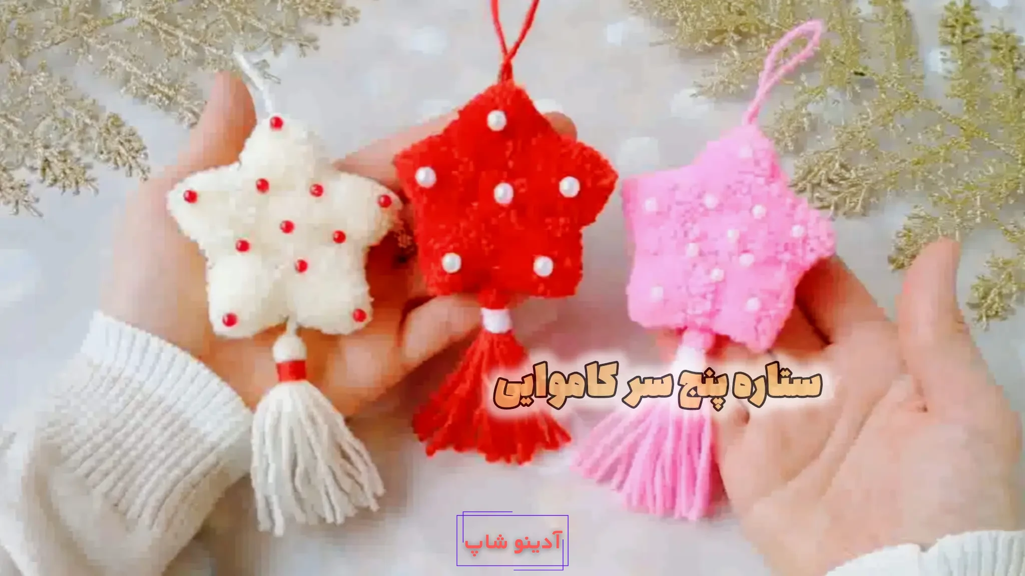 سه عدد آویز ستاره کاموایی پنج پر به رنگ‌های قرمز، سفید و صورتی با بافت مخملی، تزیین مروارید و منگوله آویز در دست.