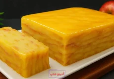 برش کیک سیب لایه‌ای فرانسوی (گاتو نامرئی) با ظاهری ژلاتینی و زرد رنگ در کنار یک سیب قرمز کامل