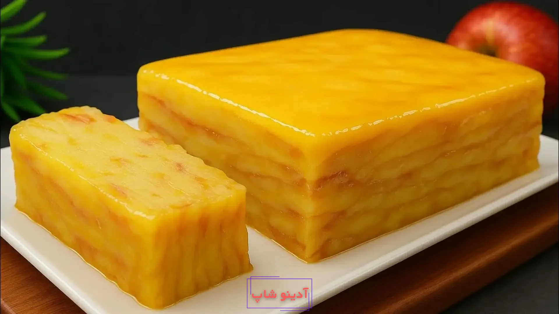 برش کیک سیب لایه‌ای فرانسوی (گاتو نامرئی) با ظاهری ژلاتینی و زرد رنگ در کنار یک سیب قرمز کامل