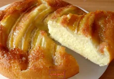 برش مثلثی از کیک موز کاراملی خانگی با بافت اسفنجی و رویه موزهای حلقه‌ای براق